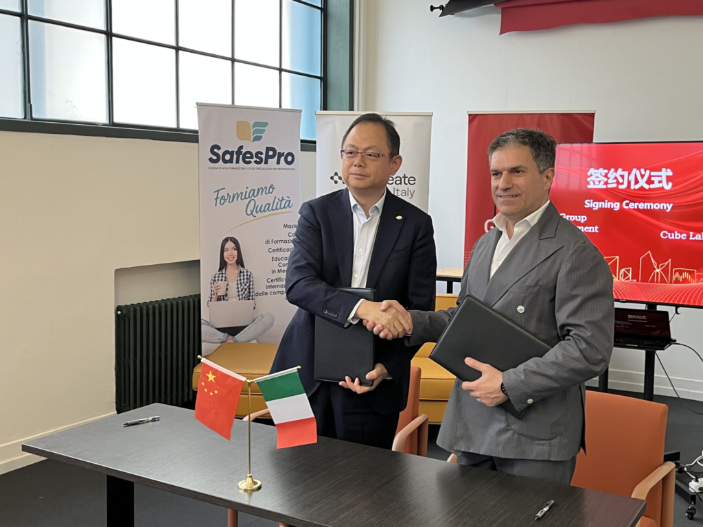 Rappresentanti di Cube Labs e Lingang Group si stringono la mano durante la firma dell'accordo di collaborazione, con le bandiere di Italia e Cina sul tavolo.